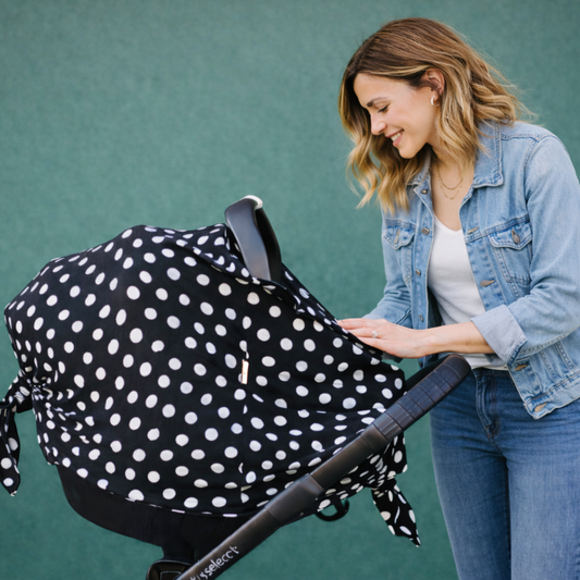 Woman looking at baby with black stroller with a white polka dot cover  with double zipper opening