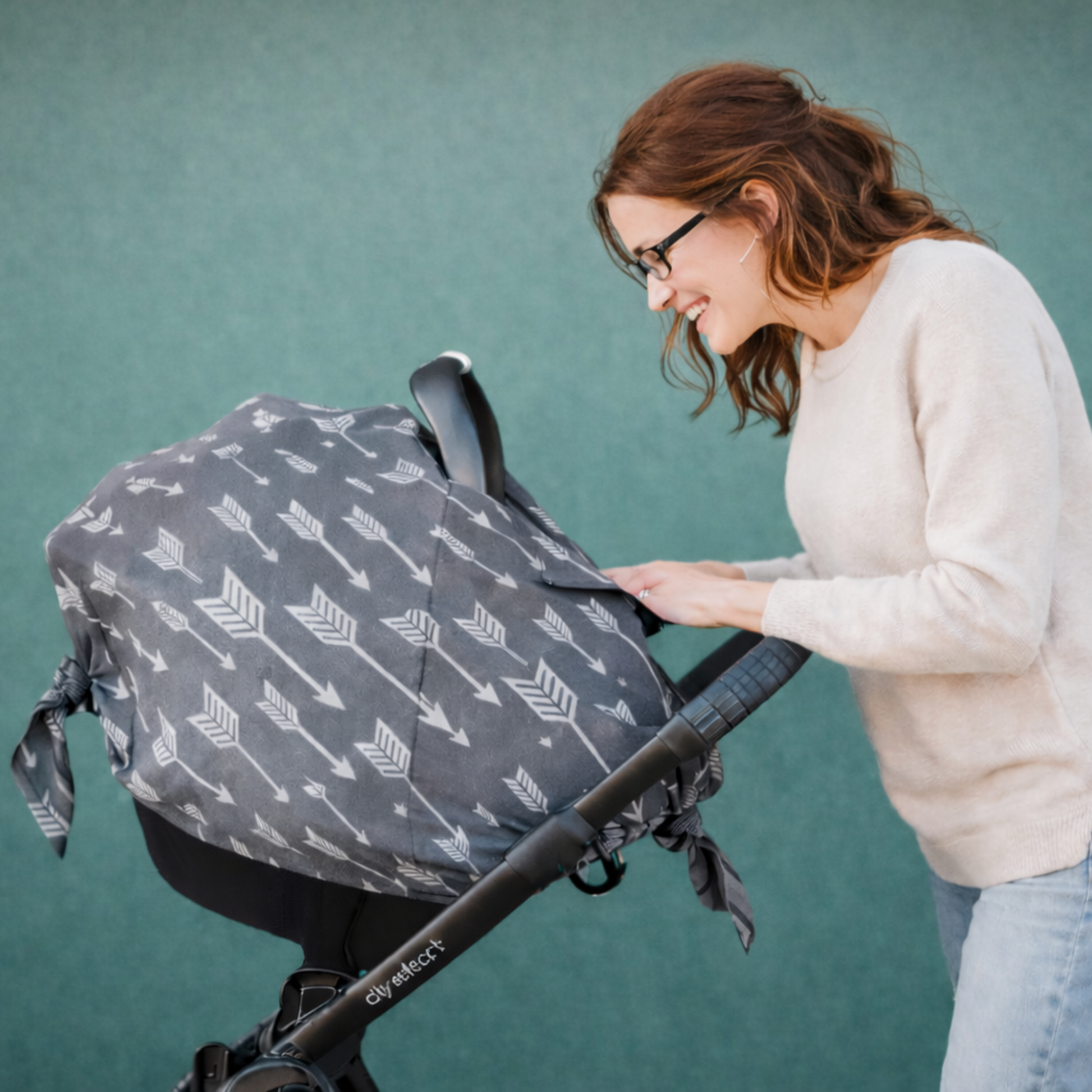 Woman adjusting a baby scar seat canopy with a arrows  patterned cover