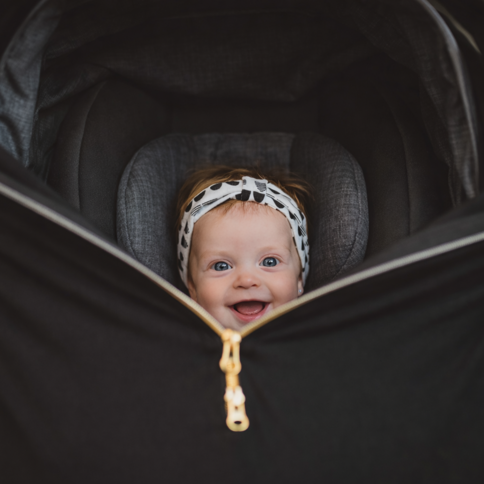 Baby peeking out from a black stroller with carseat cover with zipper