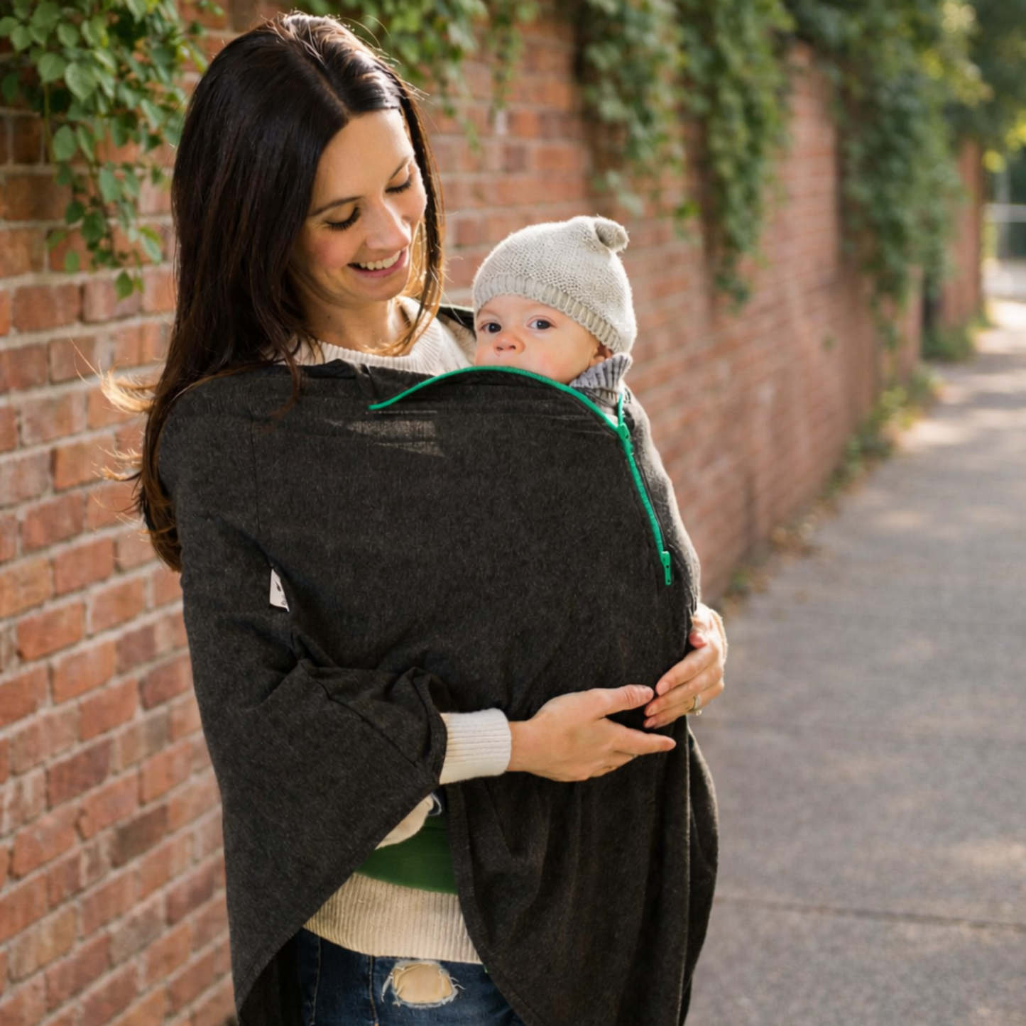 Woman carrying a baby carrier cover against a brick wall with greenery.