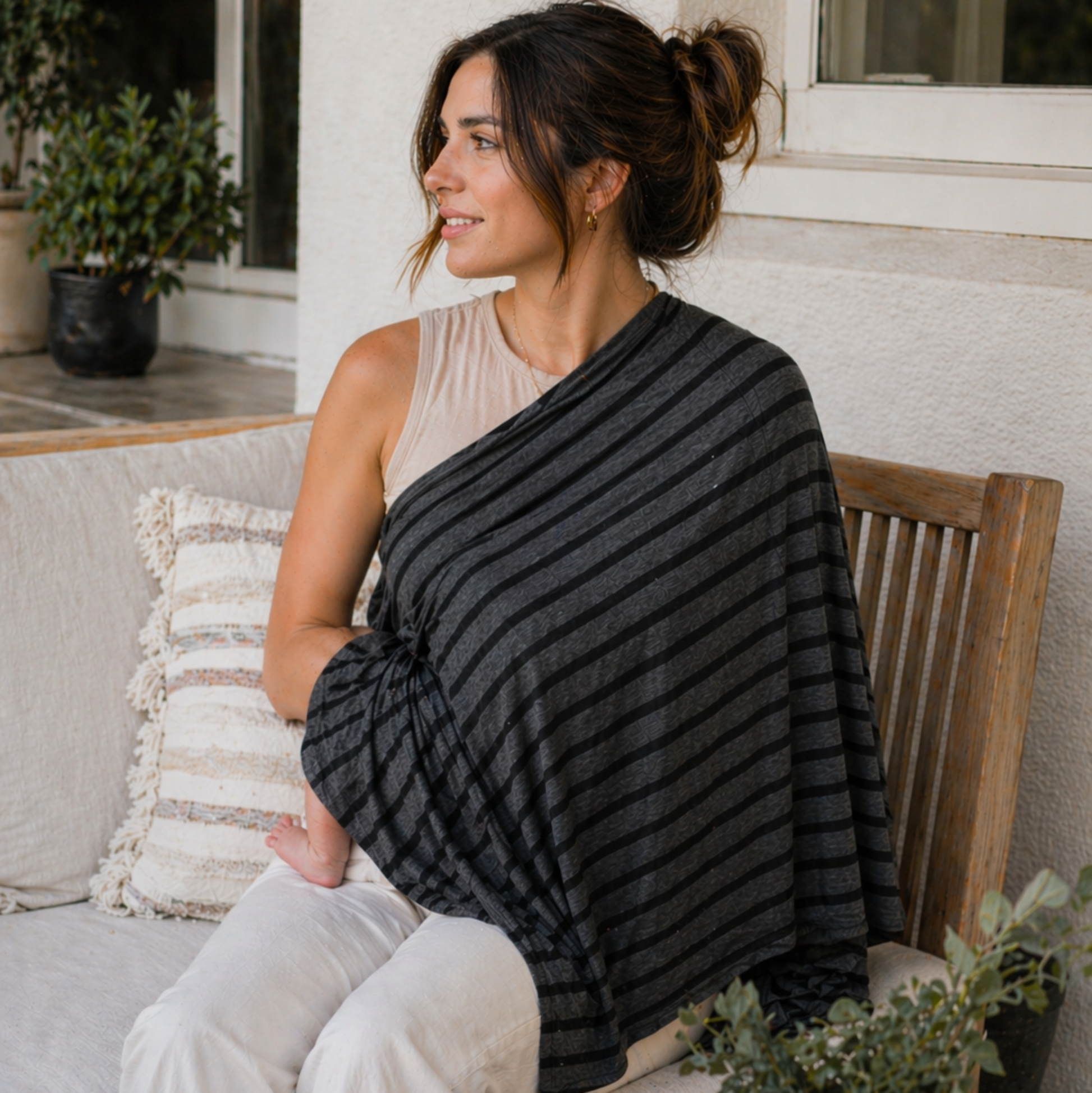 Woman sitting on a porch with a striped nursing poncho, surrounded by plants and a cup.