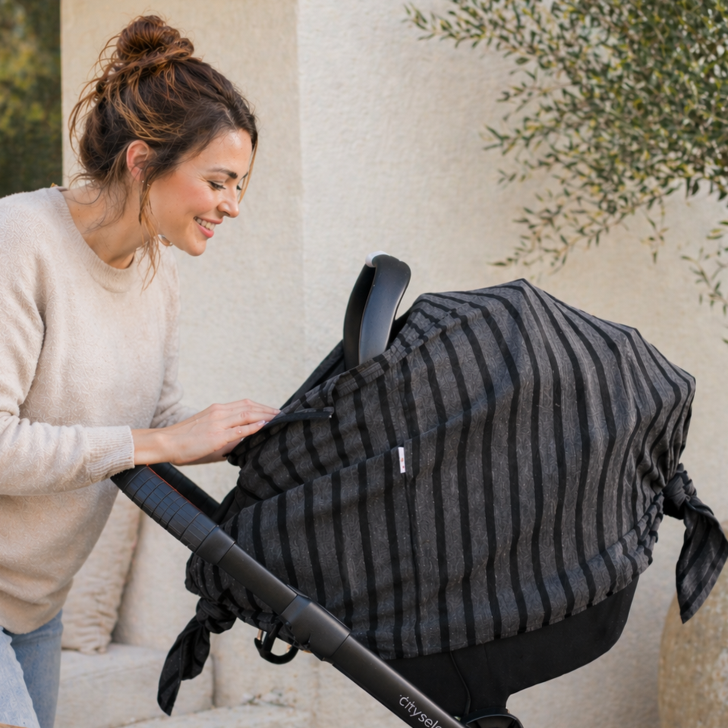 New mom with baby car seat canopy outdoors with plants in the background