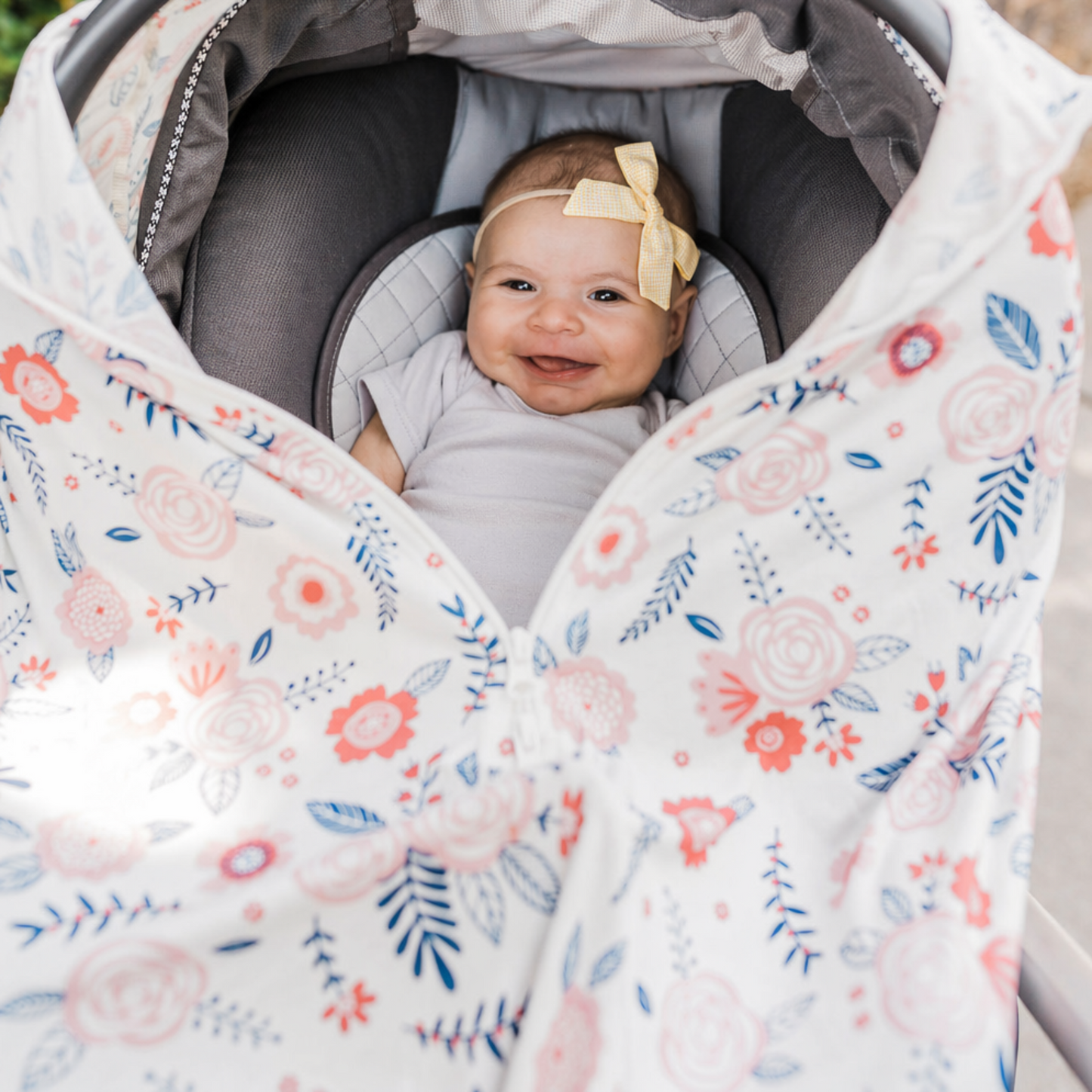 Baby in a stroller with a floral cover, surrounded by greenery
