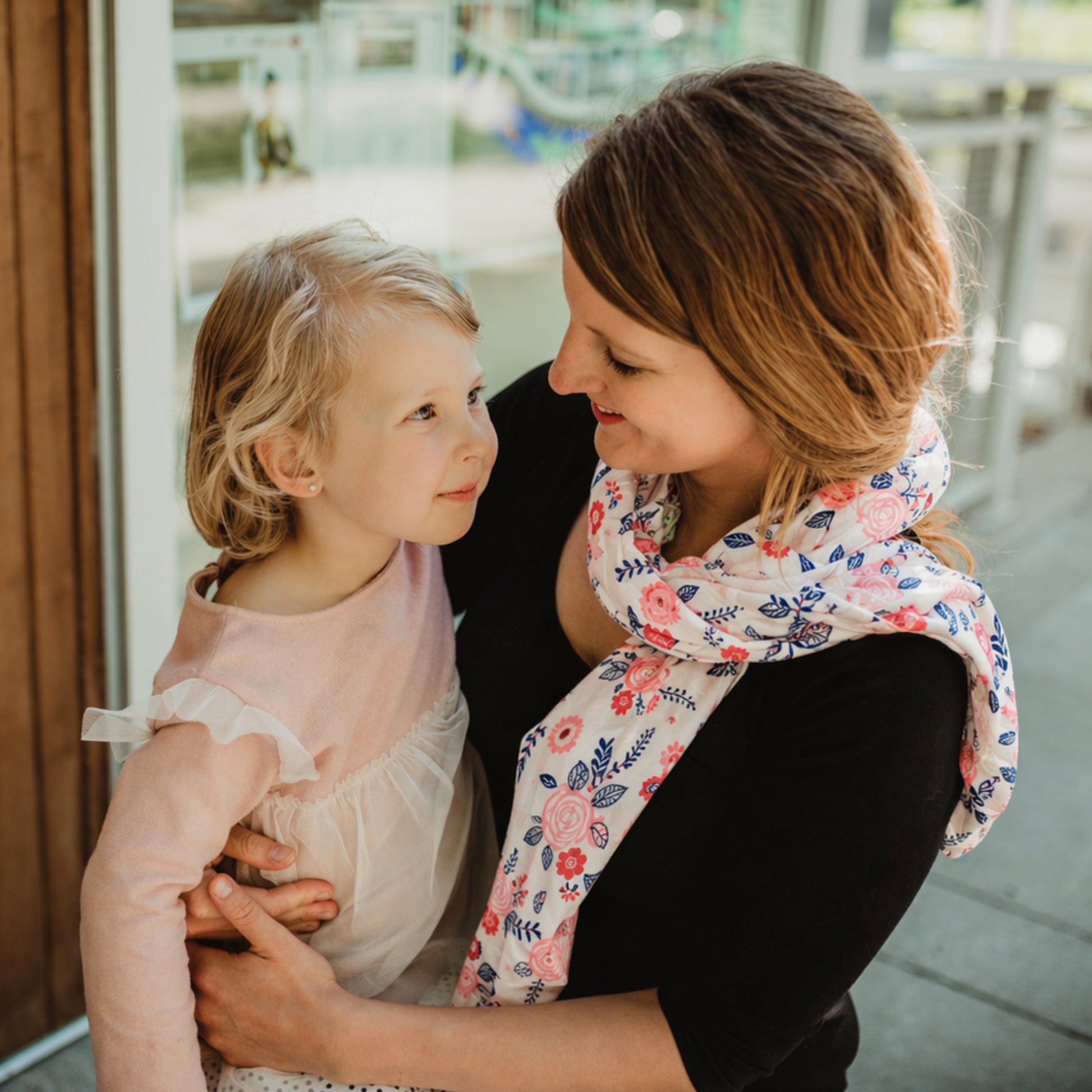 mom holding daughter by a window with a blurred outdoor background