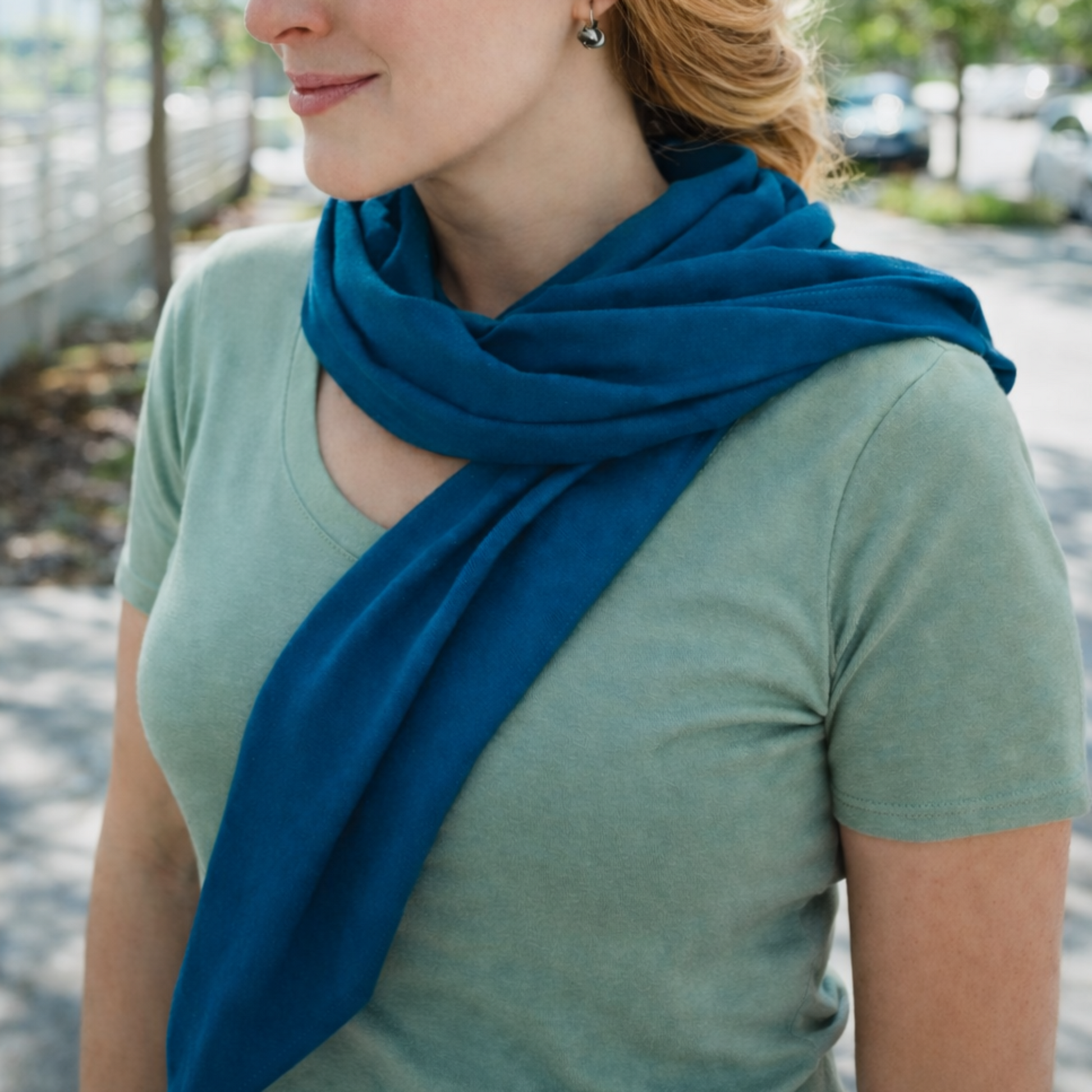 Woman wearing a blue scarf outdoors with trees and a road in the background