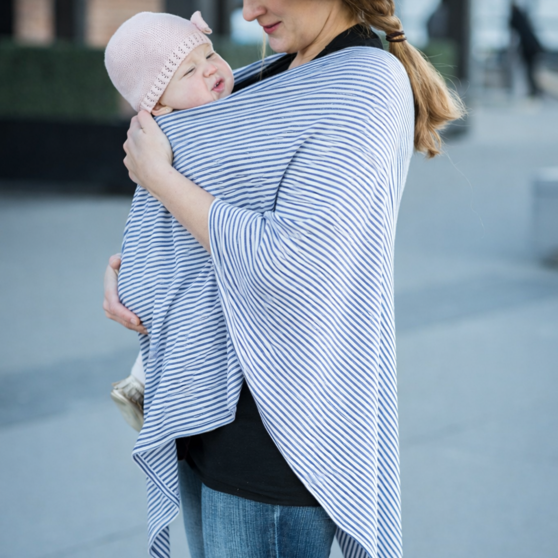Woman wearing blue and white and striped poncho, holding a baby wrapped in a carrier.