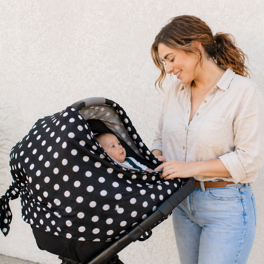 Woman holding a baby in a stroller with a black and white polka dot cover against a light background