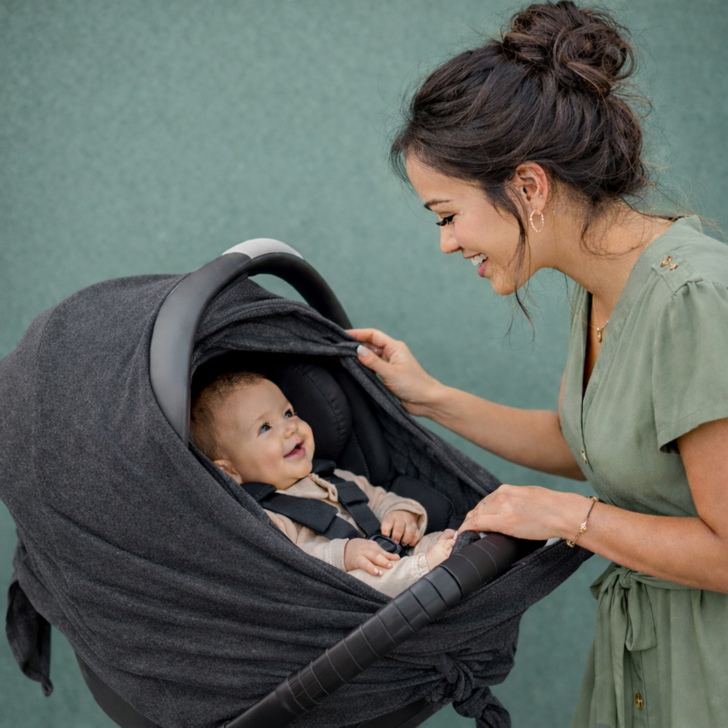 Woman adjusting a baby carrier with a smiling baby inside against a teal background