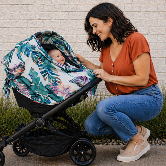 Woman adjusting a palm leaf floral-patterned stroller with a baby inside against a brick wall.